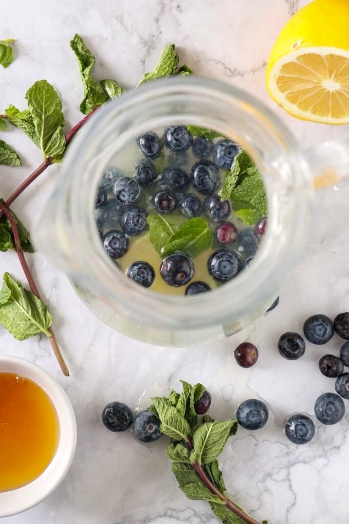 Top view of blueberries and mint leaves muddled with lime juice in a glass jar, preparing the base.