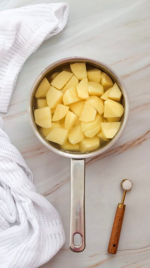 Cut potatoes soaking in a pot of salted water before boiling, preparing them for a creamy potato salad recipe.