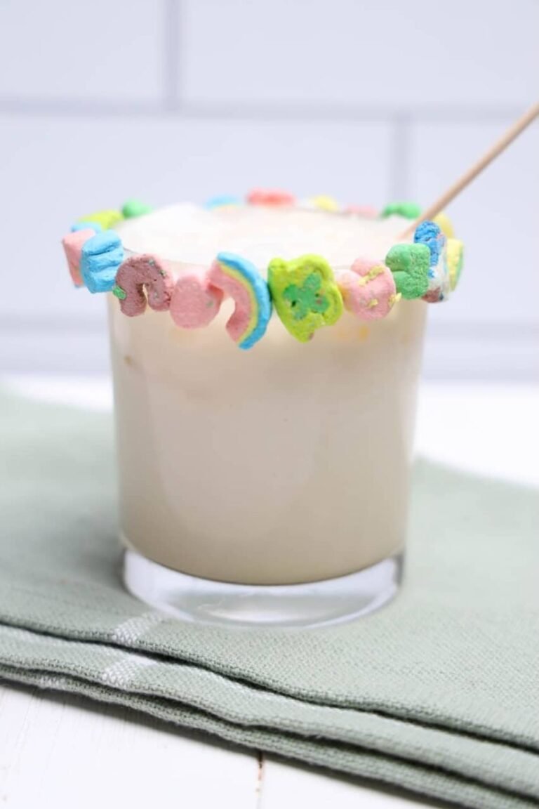 Close-up of a creamy boozy Lucky Charms drink in a glass with a colorful marshmallow rim and stir stick.