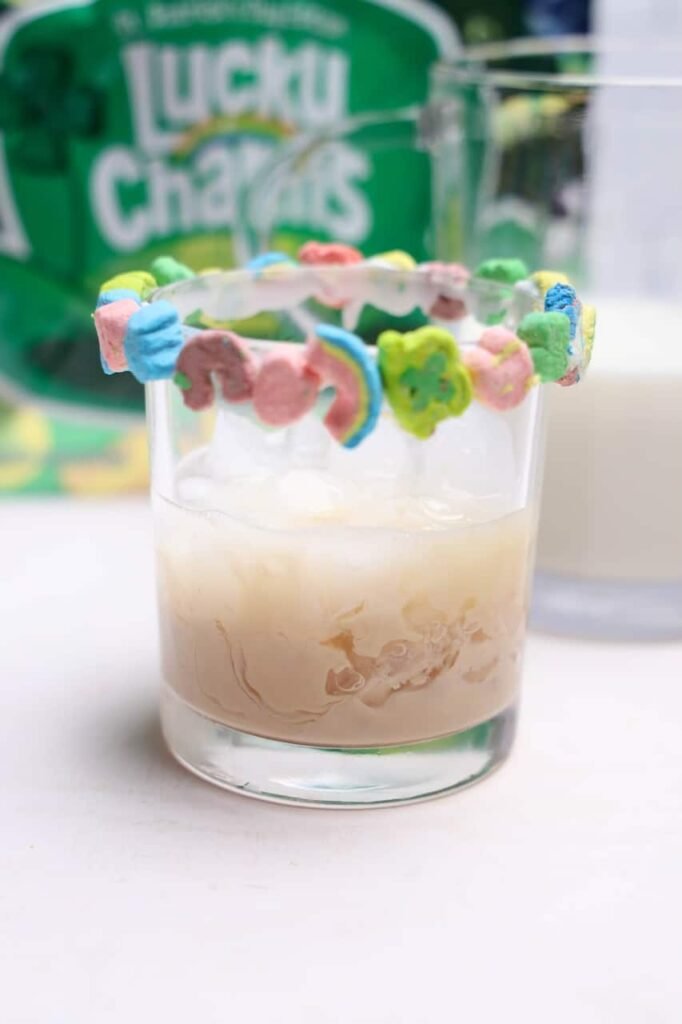 Milk being poured into a glass with Baileys over ice, topped with a cereal marshmallow rim, showing the drink mixing together.