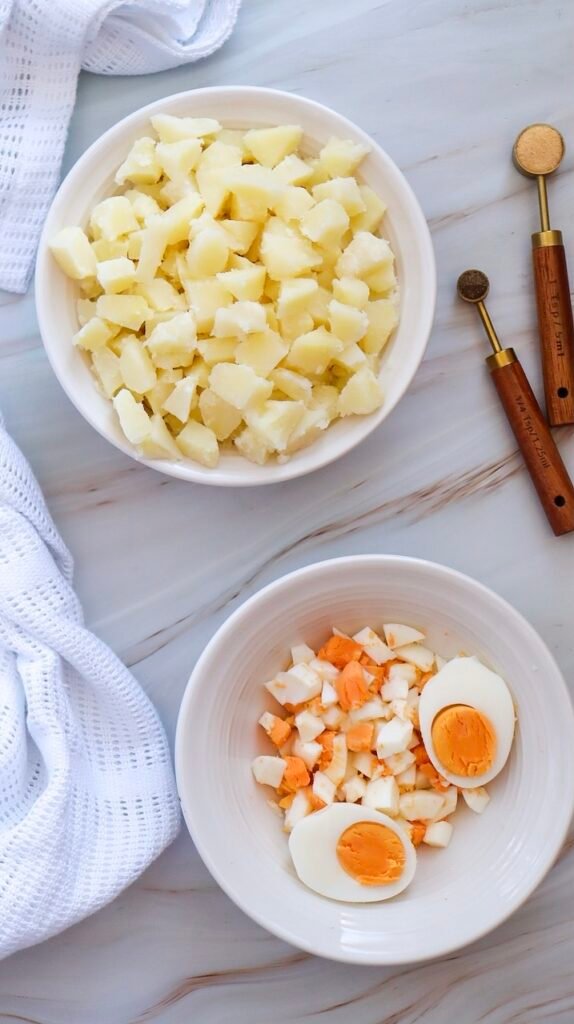 Chopped boiled potatoes in one bowl and chopped hard-boiled eggs in another, prepared for making easy side dish