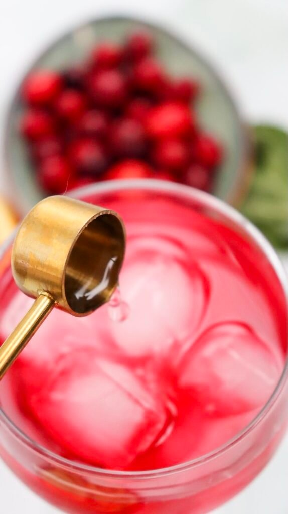 Close-up of fresh lime juice being poured into a glass of cranberry juice and ice, showing a step in making a drink.