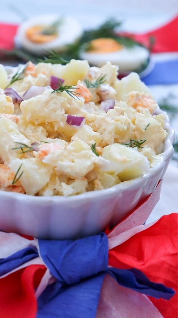 Close-up of creamy potato salad with chunks of potatoes, eggs, red onion, and fresh dill in a white bowl.