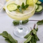 Cucumber margarita mocktail served in a glass with a salted rim, ice, cucumber slices, and fresh mint garnish on a light surface.