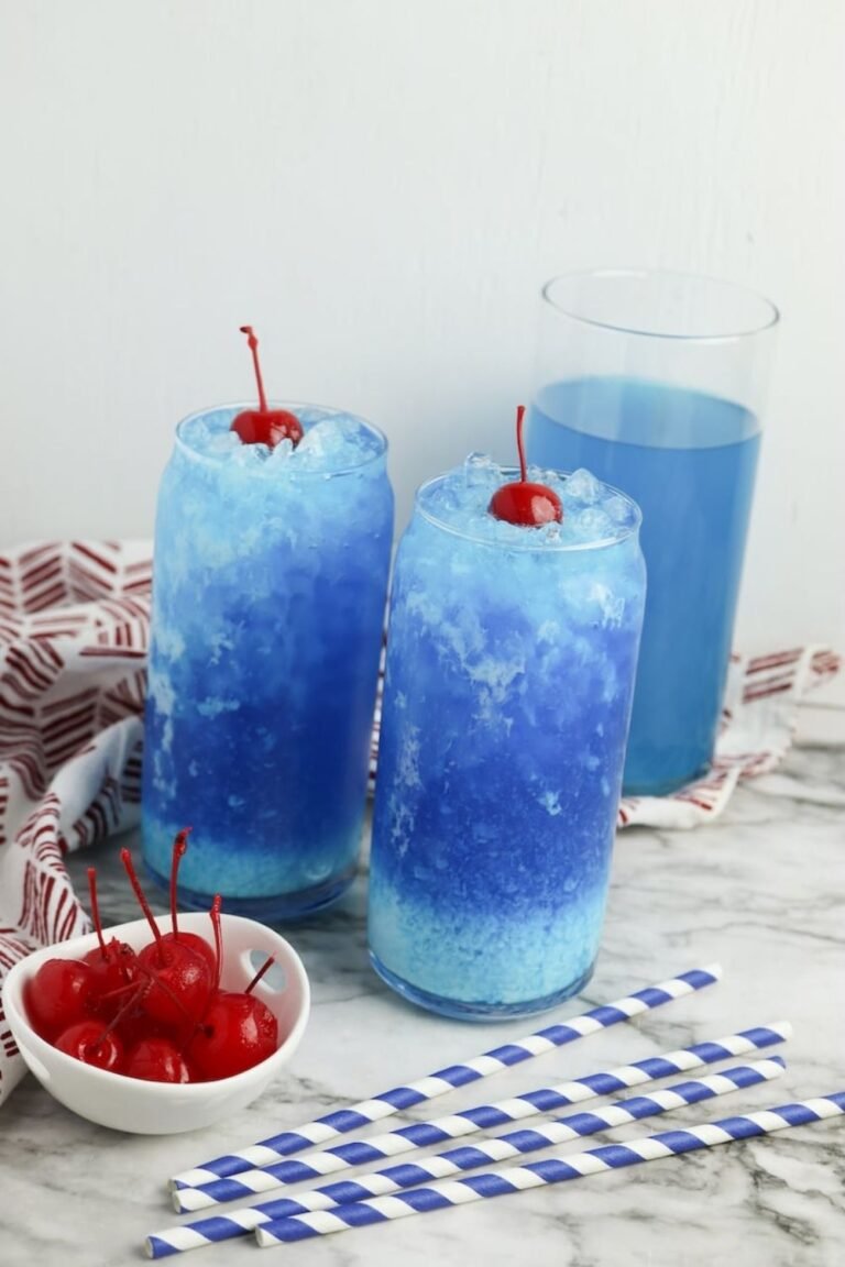 Two glasses of Dirty Ocean Water with creamy swirl and crushed ice, topped with cherries, with extra cherries and striped straws on the table