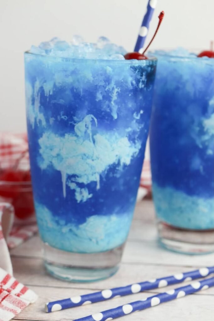 Close-up of a glass of Dirty Ocean Water with a creamy swirl, crushed ice, and a cherry garnish with a straw