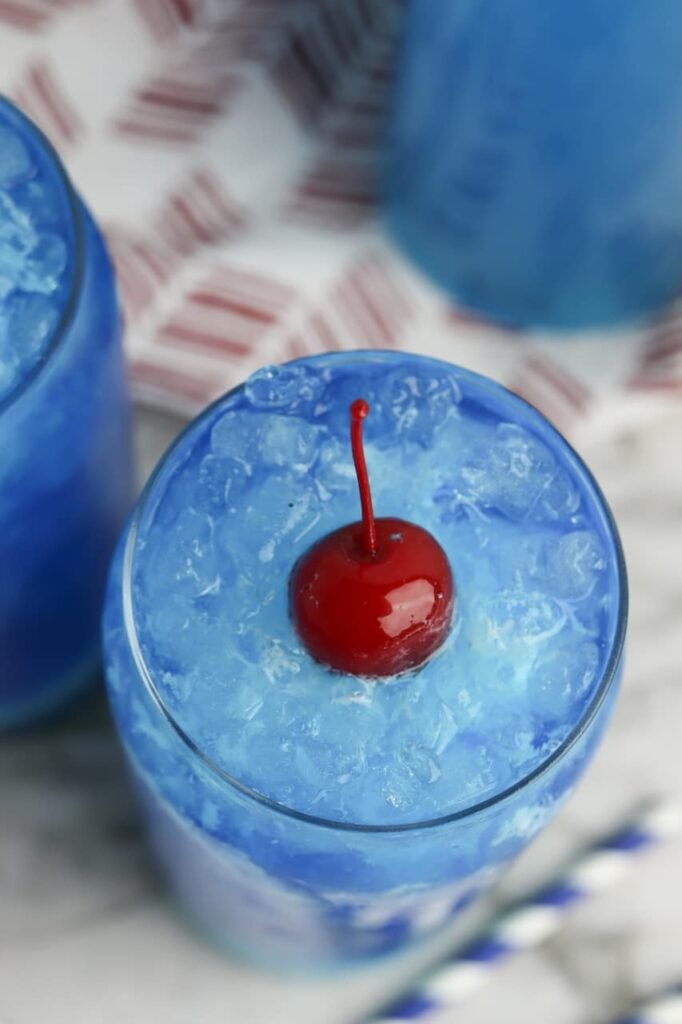 Top view of a glass of Dirty Ocean Water filled with crushed ice and a bright red cherry centered on top, showing the creamy blue swirl pattern and icy texture of the drink