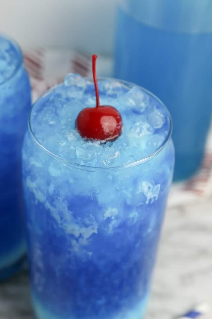 Close-up of a glass of Dirty Ocean Water with crushed ice, creamy blue swirl, and a cherry on top