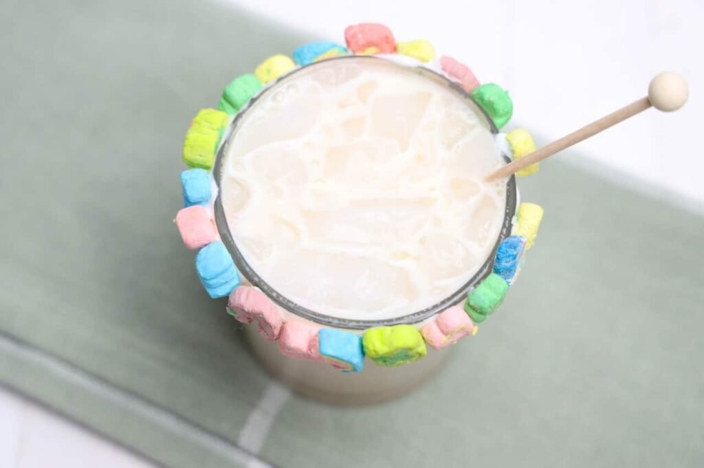 Top view of a creamy boozy Lucky Charms drink with ice and a colorful marshmallow rim in a glass.