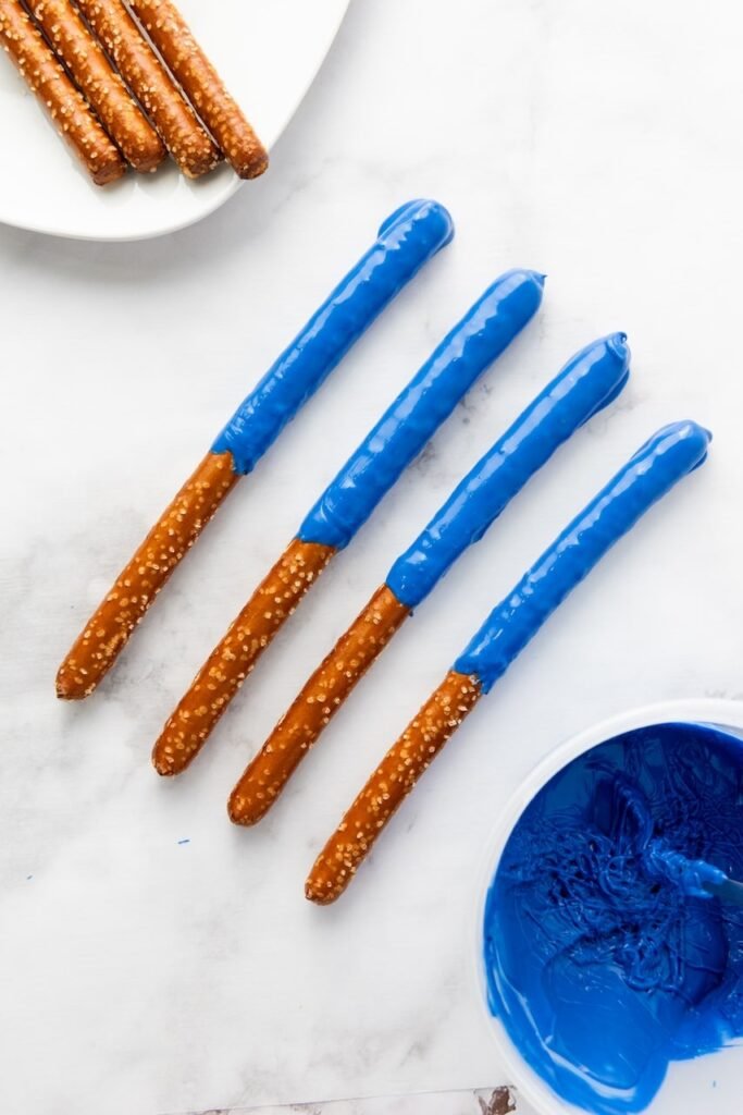 Snackpartially dipped in blue candy coating with a bowl of melted candy nearby, showing the coating step.