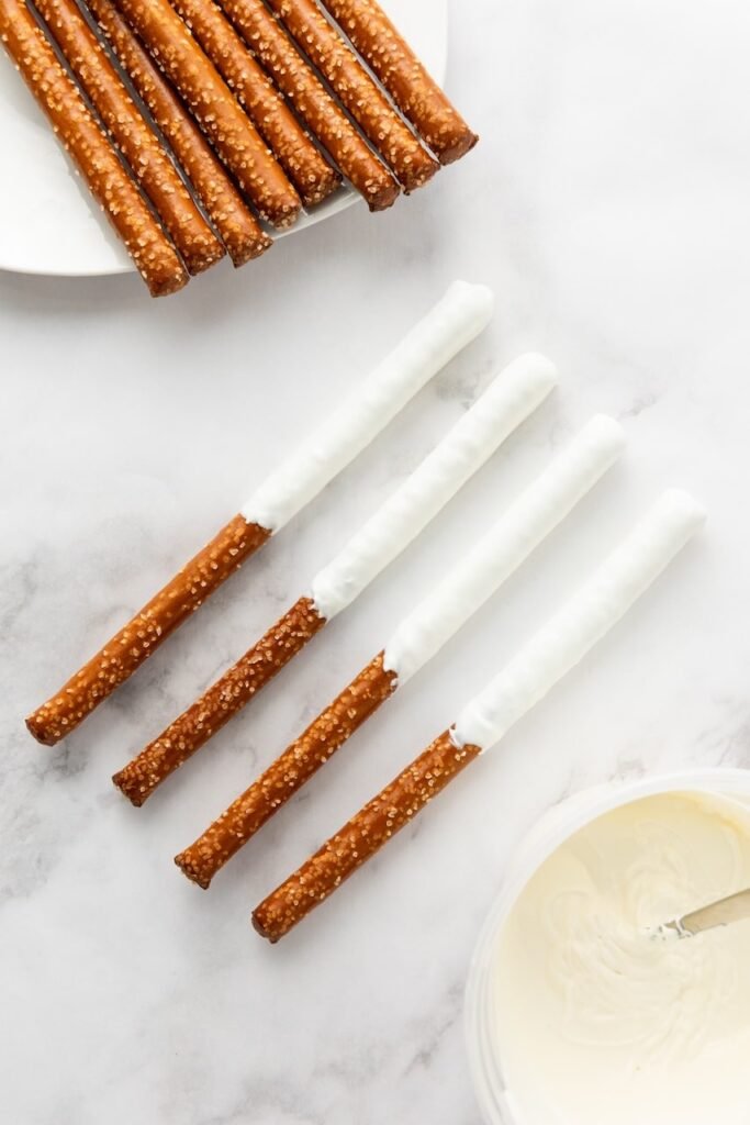 Pretzel rod being coated in melted white candy, showing part of the dipping process for firecracker pretzel rods.