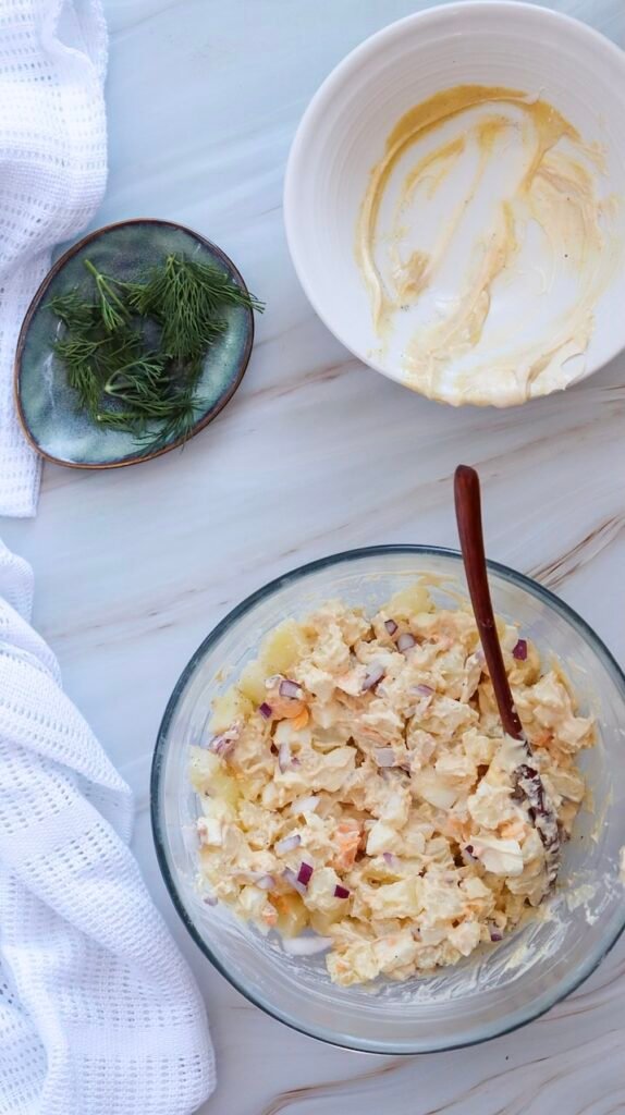 side dish being mixed in a glass bowl with chopped eggs and red onion coated in a creamy dressing.