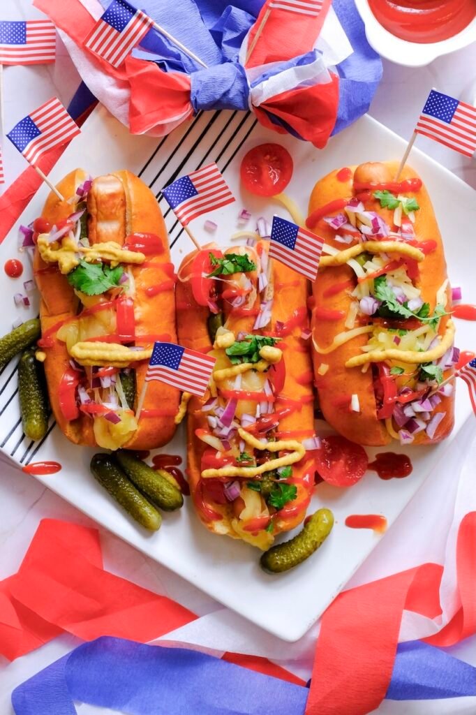 Grilled hot dogs with toppings and small American flags partially visible in a summer cookout setup.