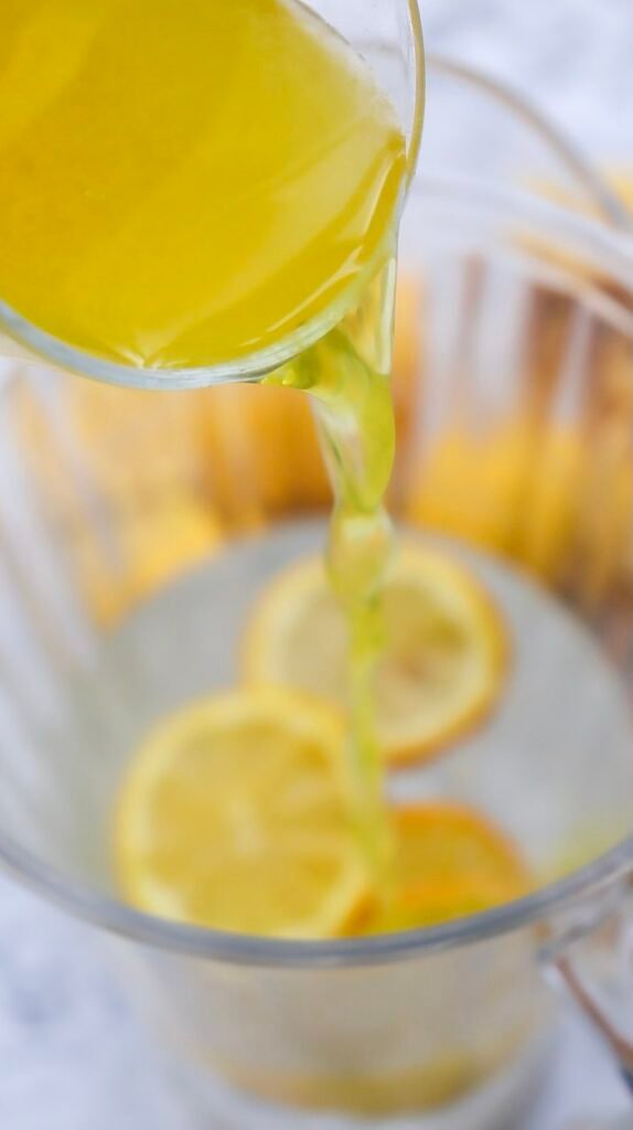 Overhead view of a pitcher filled with summer drink and floating lemon slices, surrounded by fresh lemons on a marble surface.