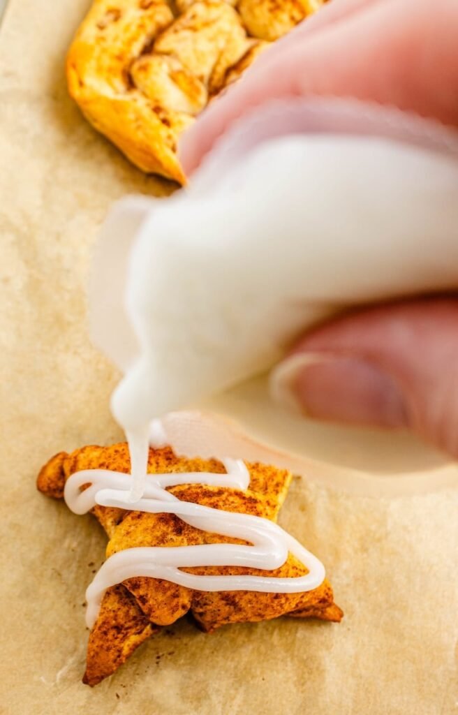 Close-up of white icing being drizzled over a warm pull apart bread on a parchment-lined baking sheet.