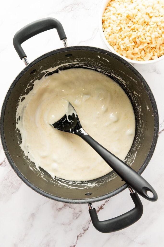 Overhead view of melted marshmallows and butter stirred together in a pot until smooth and creamy, ready for making rice krispie treats.