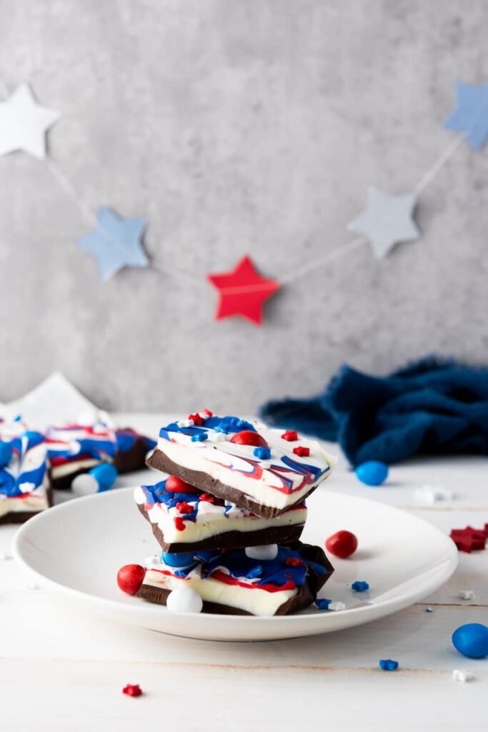 Stacked pieces of red, white, and blue chocolate bark on a white plate with star decorations in the background, styled for a 4th of July celebration.
