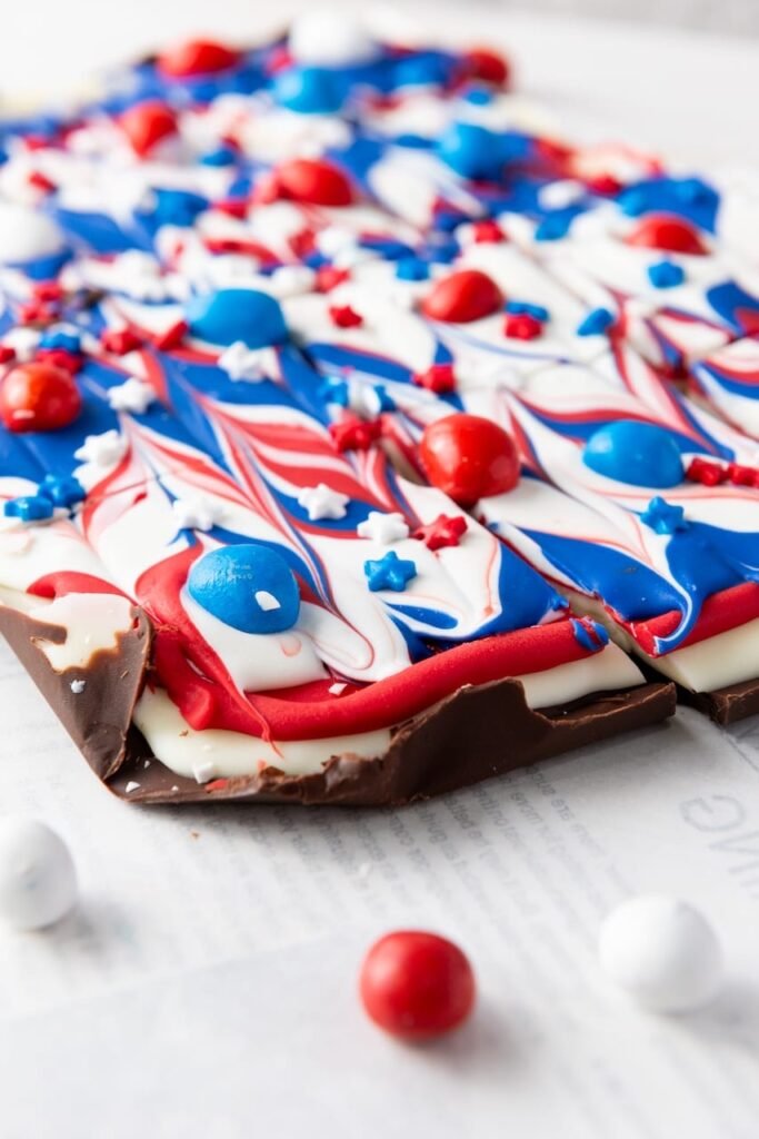 Close-up of red, white, and blue chocolate bark with swirled chocolate layers, candy-coated chocolates, and star sprinkles, showing texture and thickness.