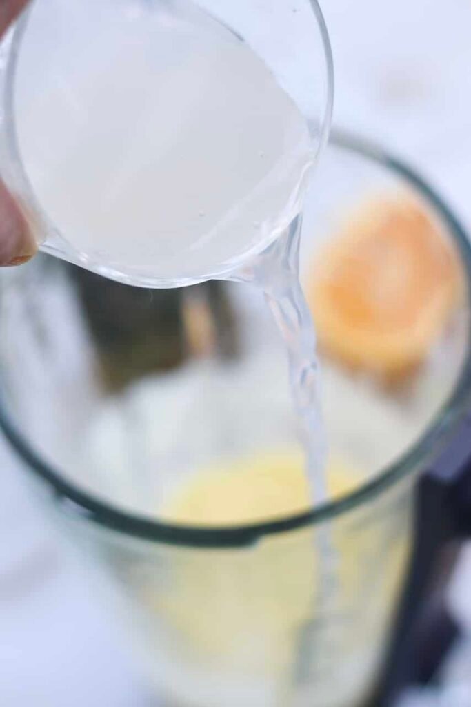 Pouring sparkling water into a blender with pineapple mixture to create a fizzy drink.