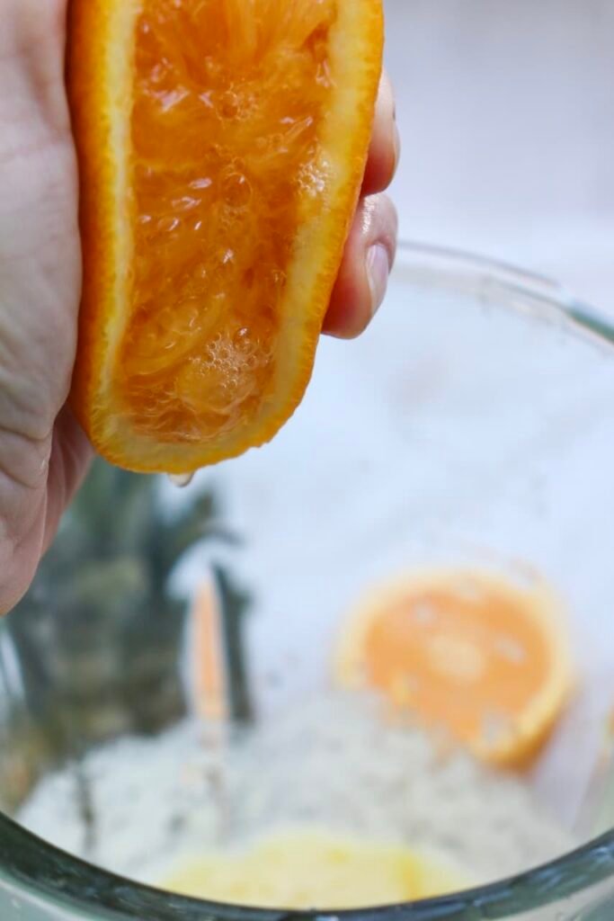 Hand squeezing fresh orange juice into a blender with pineapple mixture, showing a step in making a summer drink