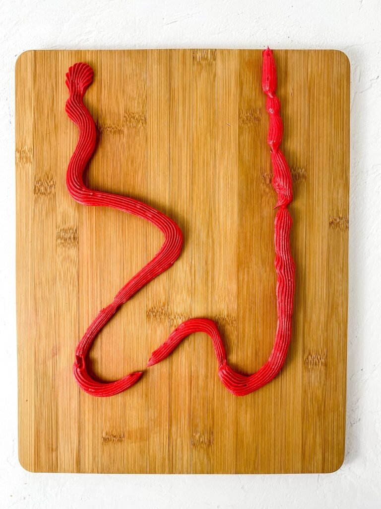 A wooden board with a decorative red buttercream frosting line piped across it, showing the first step in creating a dessert board.