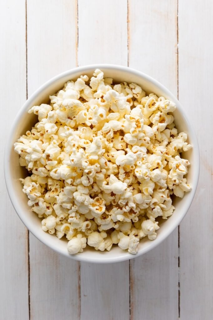 A white bowl filled with freshly popped popcorn sitting on a white wooden surface, showing light, fluffy kernels ready to be used for making 4th of July popcorn.