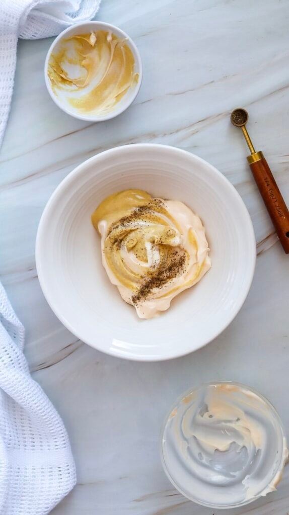 Mayonnaise and Dijon mustard mixed with seasonings in a bowl to create a creamy dressing for potato salad.