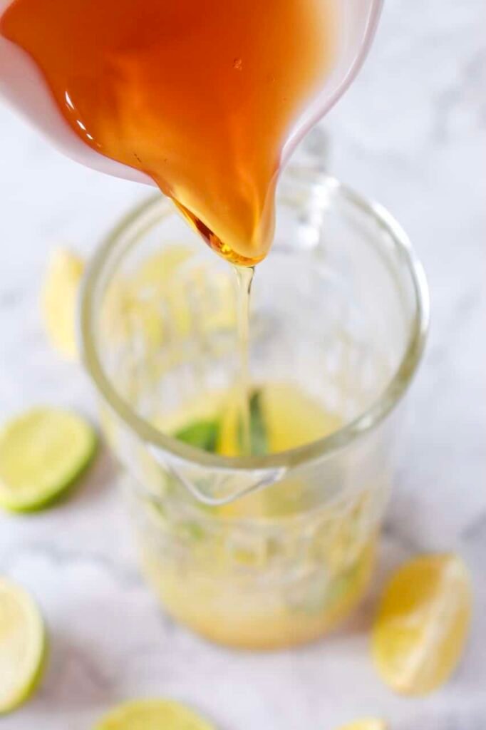 Close-up of agave syrup being poured into a glass pitcher with lime juice and mint while making a drink