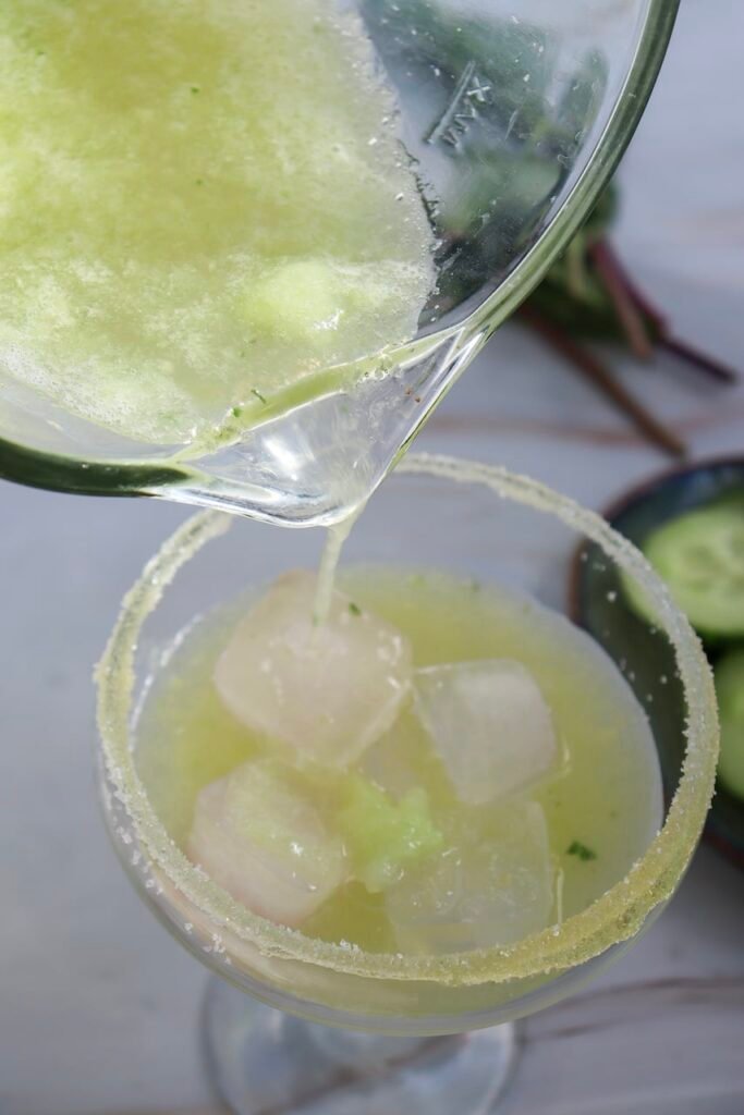 Drink being poured from a blender into a glass with a salted rim and ice, showing a refreshing non-alcoholic drink being served.