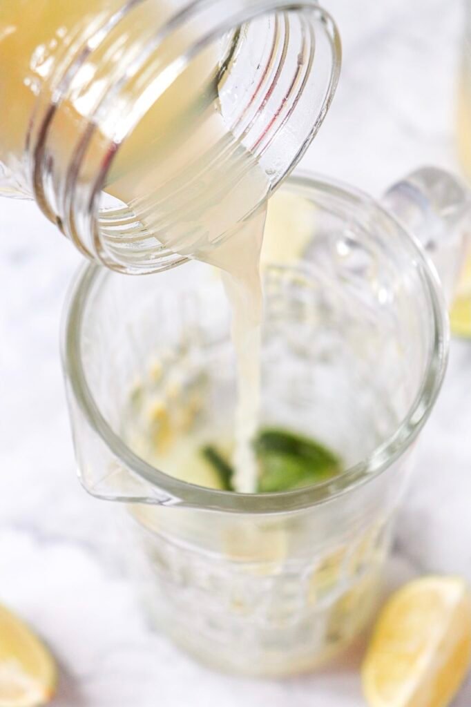 Close-up of fresh lime juice being poured into a glass jug with mint leaves while making a virgin mojito mocktail.
