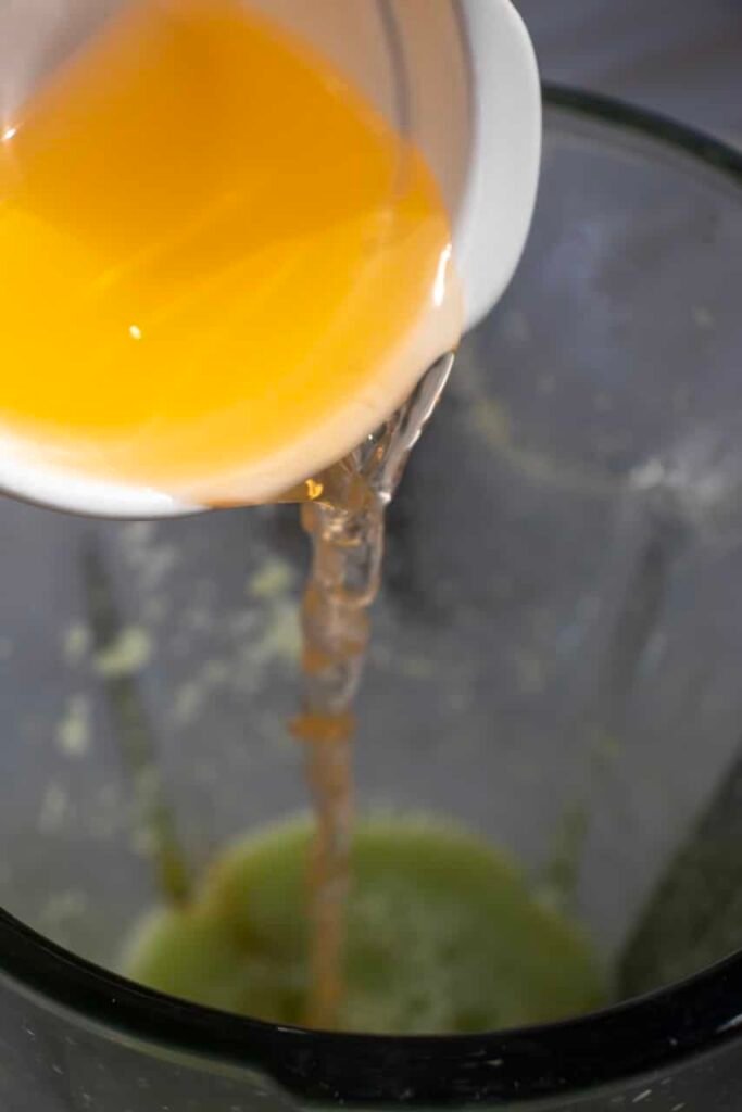Close-up of orange juice being poured into a blender with cucumber mixture while making a drink, showing a key step in building flavor.