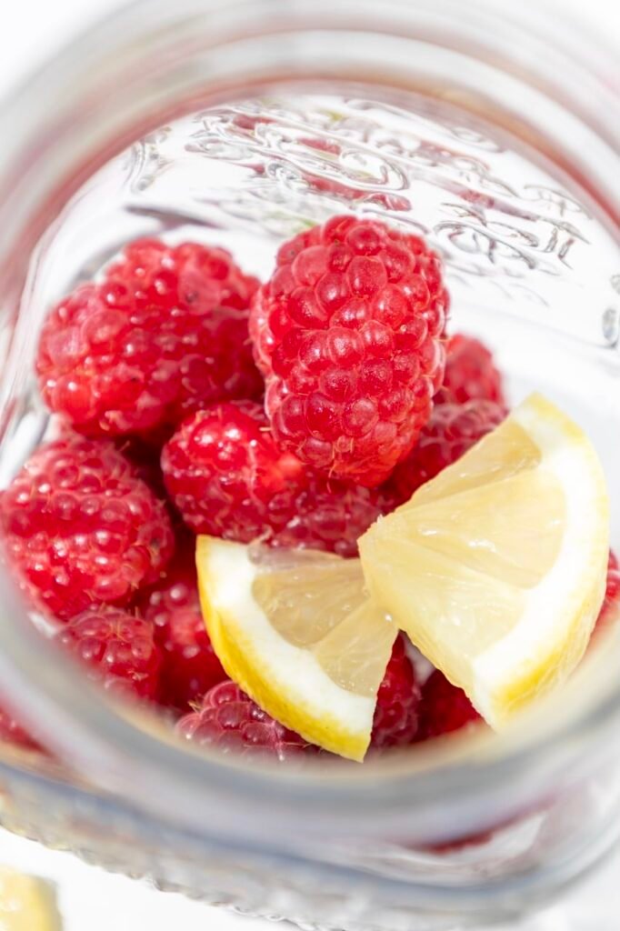 Close-up view of fresh raspberries and lemon slices inside a glass jar, showing the base ingredients before mixing.