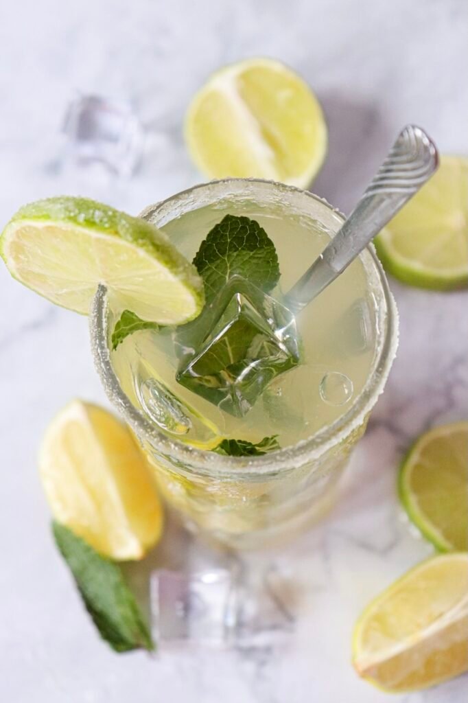 Top view of a virgin mojito mocktail in a glass with ice, mint leaves, and a lime slice garnish on a marble surface.