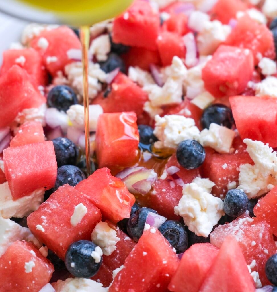 Close-up of watermelon feta salad with blueberries and red onion as olive oil is drizzled over the top.