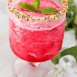 Glass of watermelon slushie with a colorful sprinkle rim and fresh mint garnish, showing the finished drink ready to serve