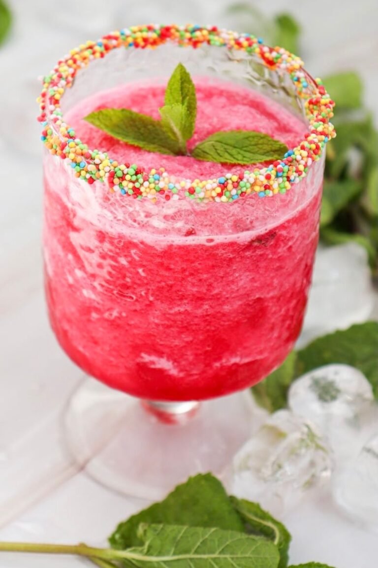 Glass of watermelon slushie with a colorful sprinkle rim and fresh mint garnish, showing the finished drink ready to serve