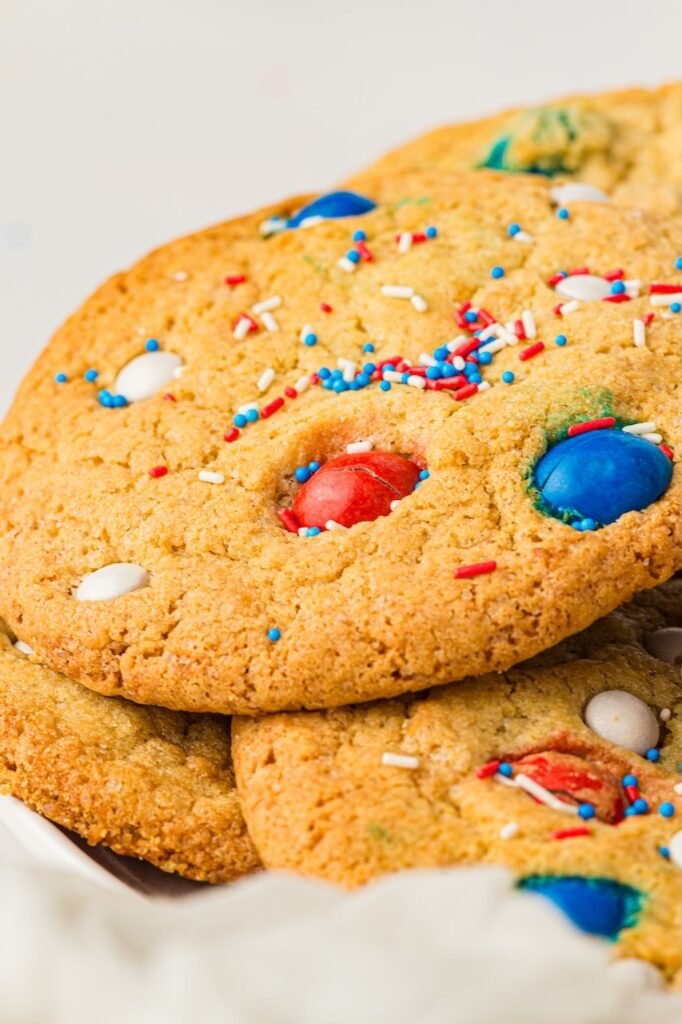 Close-up of soft and chewy 4th of July cookies stacked together with red, white, and blue M&Ms and patriotic sprinkles baked into the tops. The homemade patriotic cookies have golden brown edges, bakery-style texture, and colorful candy pieces perfect for summer holiday dessert tables and Independence Day parties.