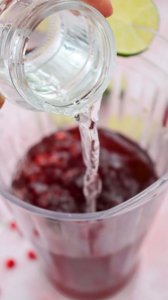 Sparkling water being poured into a pitcher with fresh lime slices in the background.