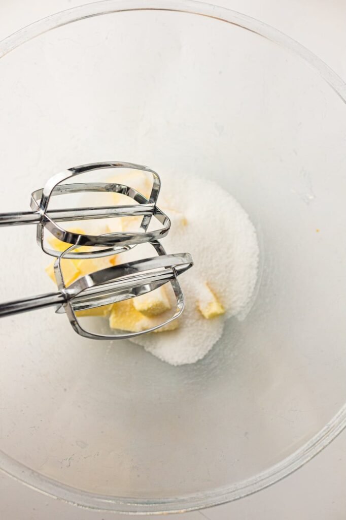 Hand mixer beaters positioned over butter and sugar in a glass bowl before mixing cupcake batter.