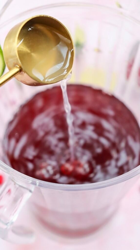 Soda water being poured into a glass pitcher filled with pomegranate juice to make non alcoholic drink.