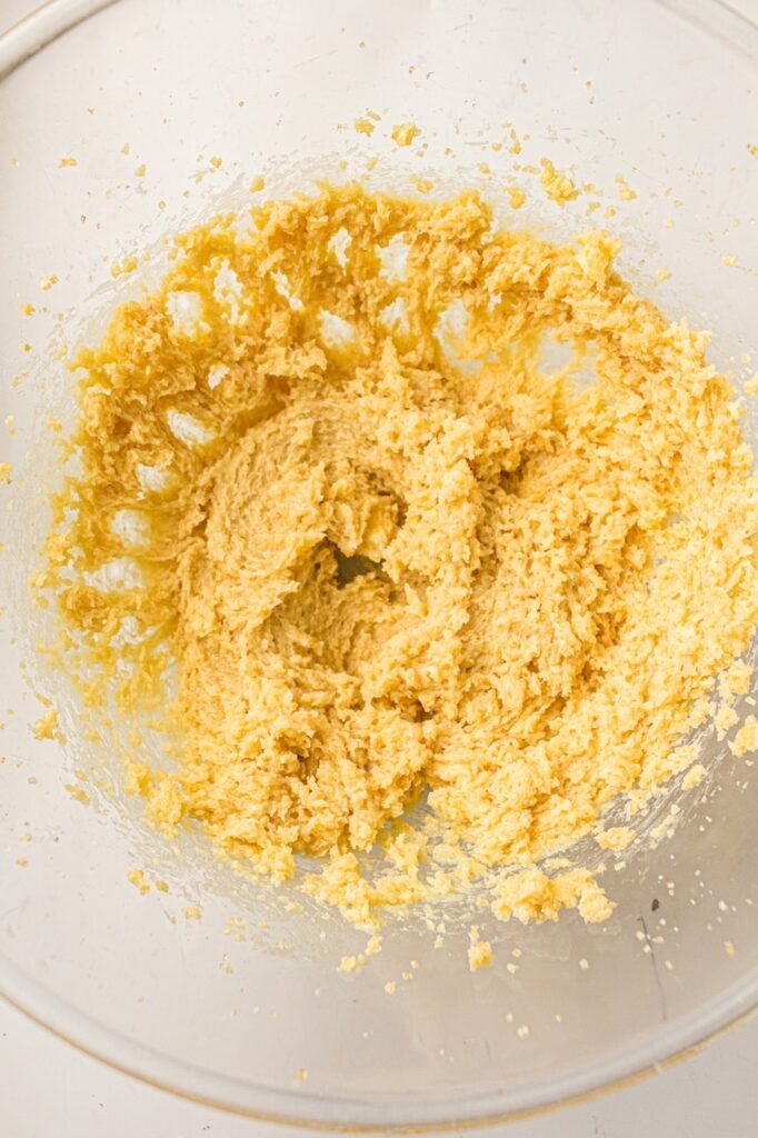 Close-up overhead view of butter, brown sugar, and white sugar creamed together in a large glass mixing bowl until light, fluffy, and pale yellow for homemade 4th of July M&M cookies. The whipped mixture has a soft, airy texture that helps create chewy bakery-style patriotic cookies with tender centers and crisp edges.