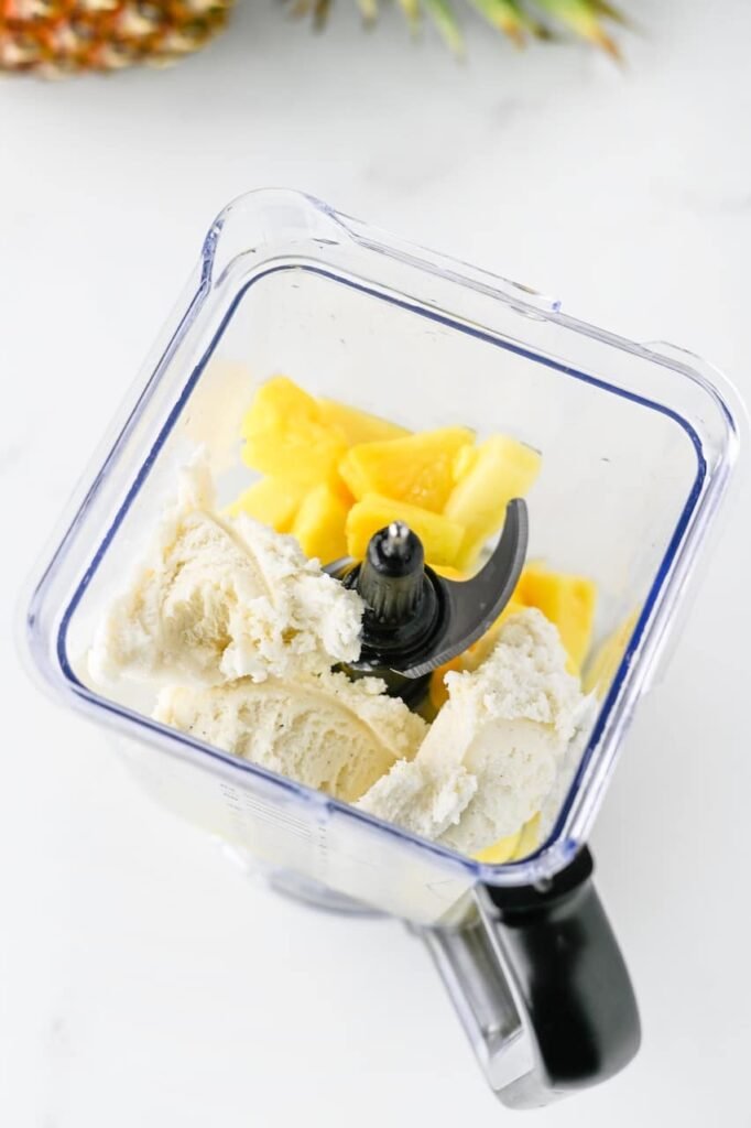 Frozen pineapple chunks and vanilla ice cream added to a blender container as the first step in making homemade disney inspired soft serve