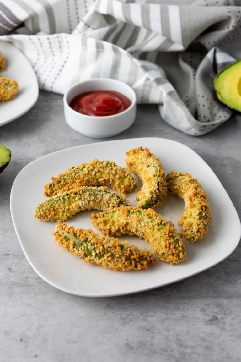 Golden brown Air Fryer Avocado Fries arranged on a white plate and served with a dipping sauce. The avocado wedges are coated in a crispy breadcrumb crust and cooked until crunchy on the outside while remaining creamy and tender inside, ready to serve as an appetizer or snack.