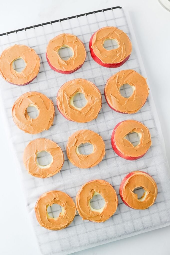 Overhead view of snack  spread with peanut butter and arranged on a wire rack, preparing them for toppings.