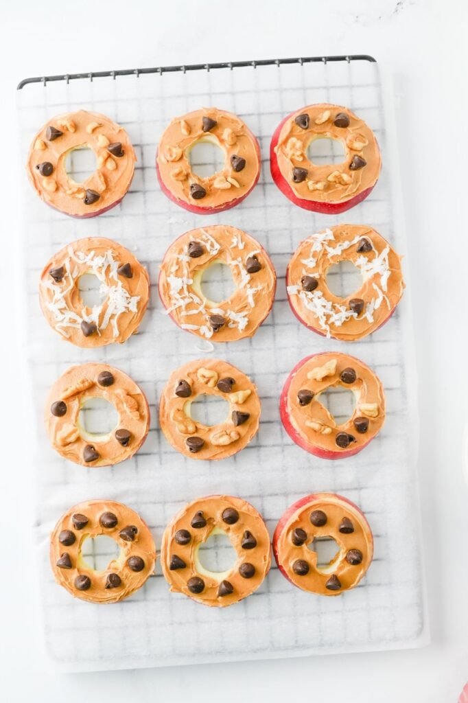 Overhead view of snack topped with peanut butter, chocolate chips, sweetened coconut flakes, and walnuts on a wire rack before serving.