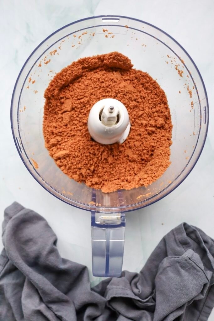 Overhead view of finely crushed cookie crumbs in a food processor, prepared for making the crust of a no-bake dessert.