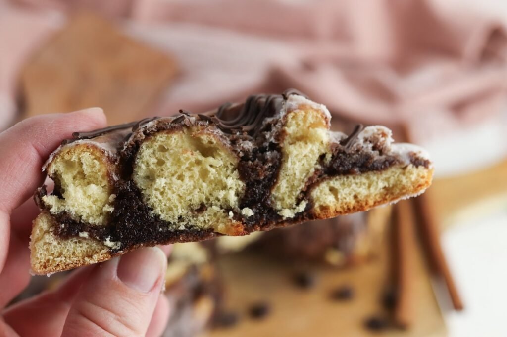 Close-up of the inside of a brownie cinnamon roll being held by hand, showing the soft fluffy cinnamon roll layers and thick fudgy brownie filling baked between each swirl. The cross-section highlights the gooey chocolate center and tender texture of the finished rolls.