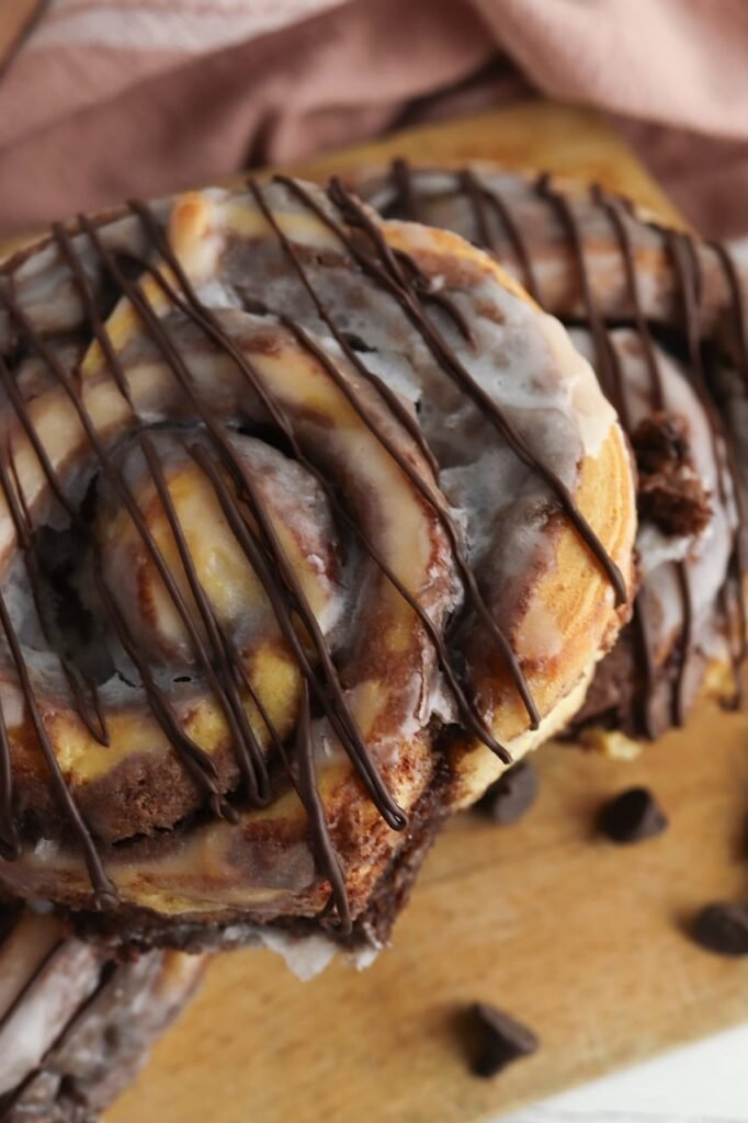 Close-up of finished brownie cinnamon rolls topped with icing and a drizzle of melted chocolate. The soft baked rolls show rich brownie filling swirled between the layers, highlighting the gooey texture and fudgy chocolate center.
