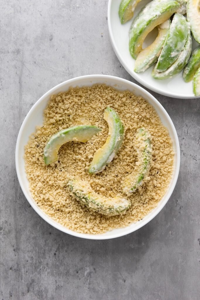 wedges coated in flour and soy milk are being covered in seasoned panko breadcrumbs before air frying. This final breading step creates a crispy outer coating that turns golden brown while the fruit stays creamy and tender inside.