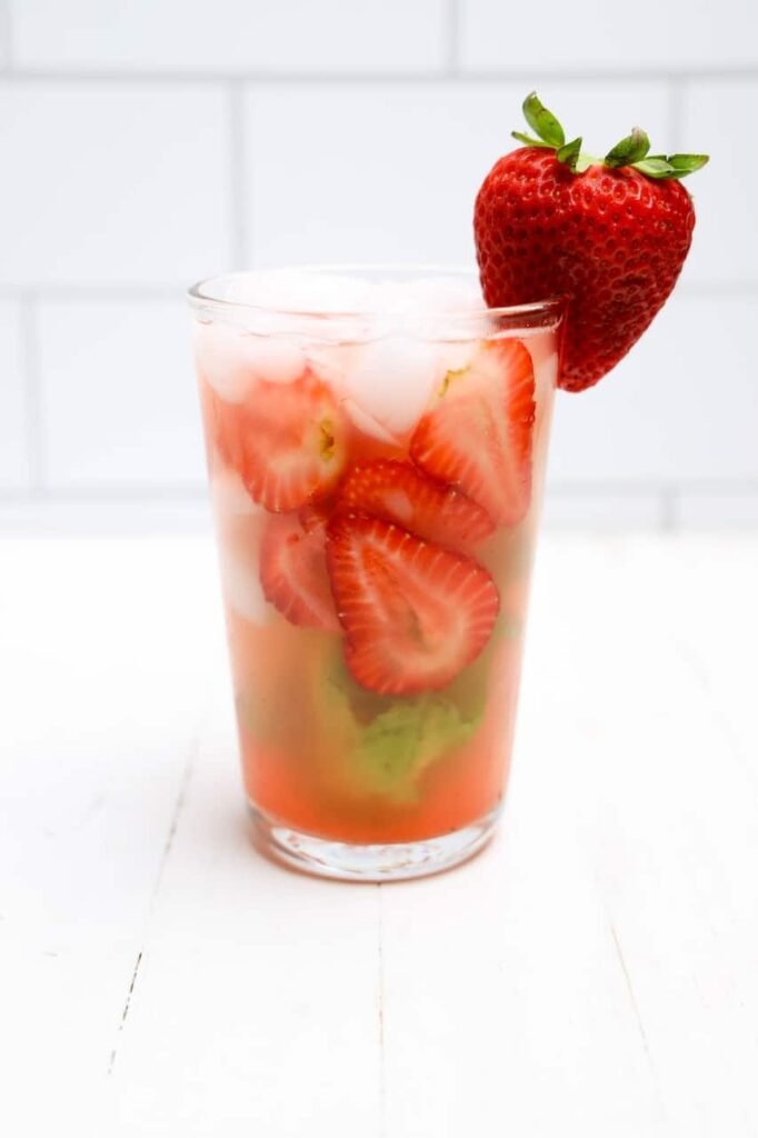 Glass of filled with sliced strawberries and ice, garnished with a fresh strawberry on the rim.